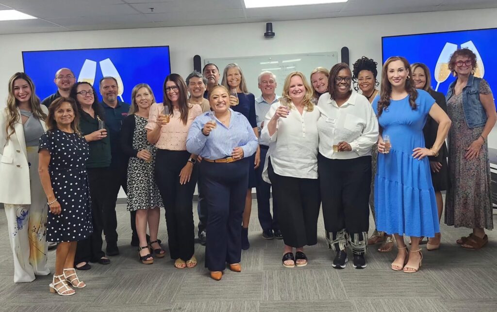 Desert Fast Pitch participants, their support people, and RAP Foundation staff pose during semifinal practice, several raising glasses in a toast.